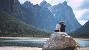 couple sitting on a rock facing mountains 